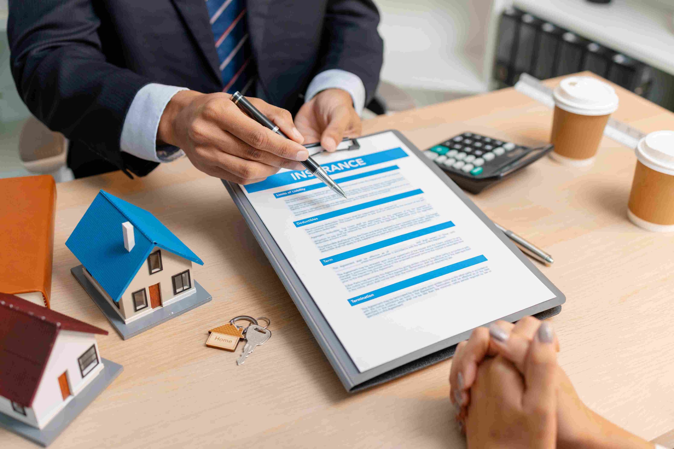 Insurance agent reviewing policy documents with a client at a desk with a calculator and model houses.