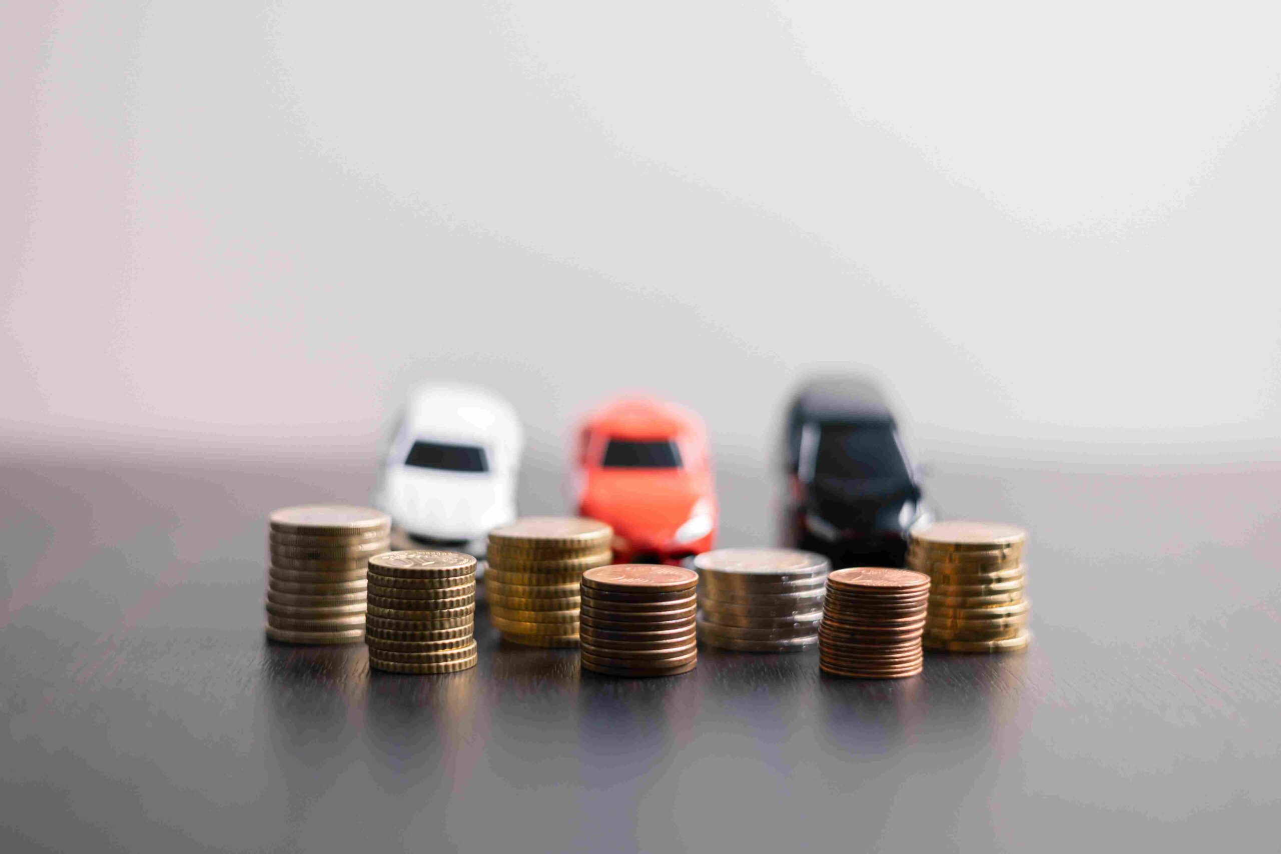 Stacks of coins arranged in front of three miniature cars, representing changing auto insurance costs.