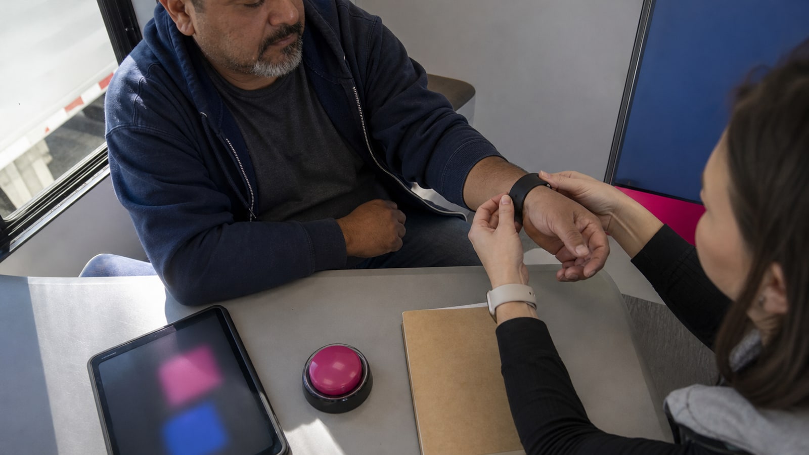 Overhead view of a researcher fitting a sleep sensor on a truck driver's wrist in a mobile lab