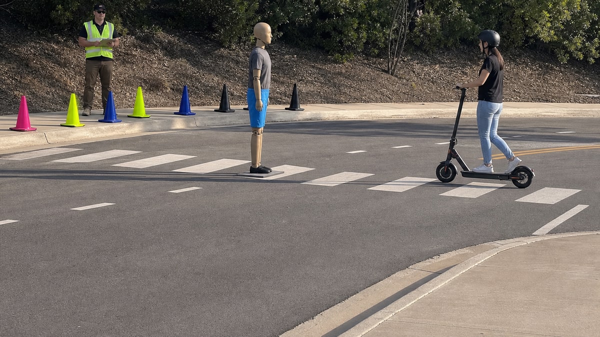 Pedestrian test dummy in a crosswalk as an e-scooter approaches on a closed street course