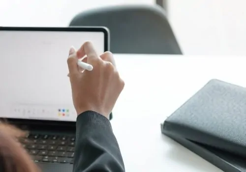 A person uses a stylus on a tablet at a desk, symbolizing digital tools that support human rights campaigns