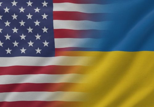 A digitally blended image showing the United States flag on the left and the Ukraine flag on the right, both waving in the wind. The transition between the two flags is smooth and slightly blurred in the center, symbolizing unity and partnership. The fabric texture is visible, and the lighting highlights the folds and motion of the flags