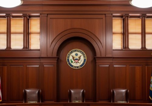 Empty courtroom with wooden paneling, featuring three brown leather chairs, the U.S. flag, and a "Court of Appeals" seal