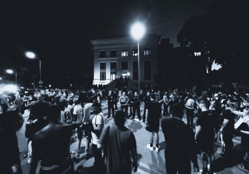 A large crowd gathers at night outside a building during a political rally as police stand in formation facing the protesters