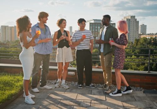 A group of friends enjoys a rooftop gathering, cocktails in hand, as the sun sets over the city