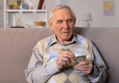 Older man counting money on a sofa