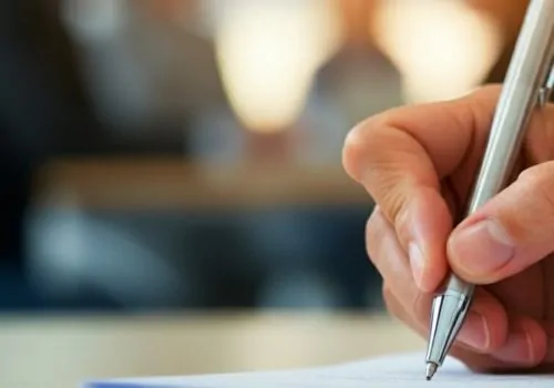 Human hand holding a pen and writing on paper