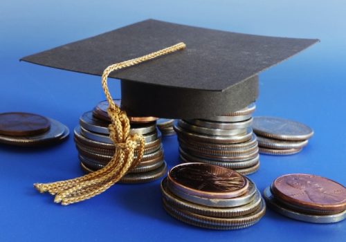 Graduation cap placed on stacks of coins representing student costs and repayment plans