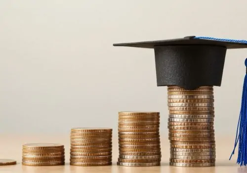 A graduation cap rests atop stacks of coins