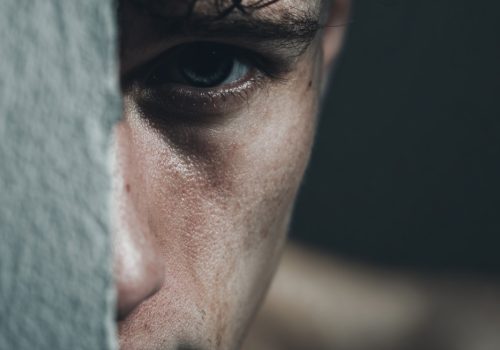 Close-up of a person’s face partially hidden behind a wall, focusing on a serious eye